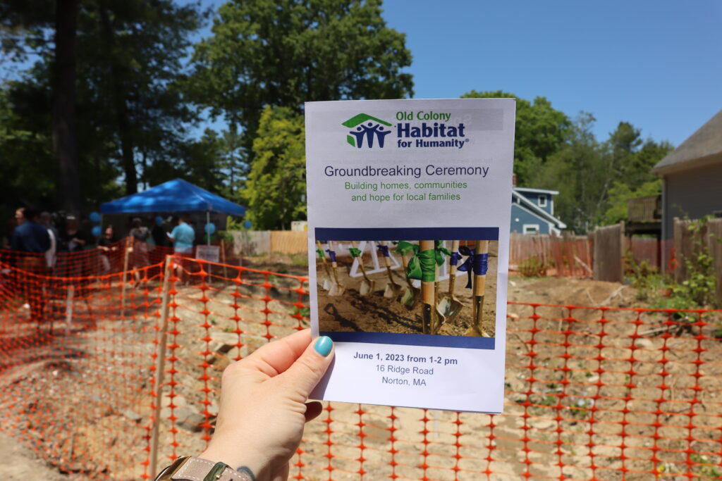 The program from the Habitat for Humanity groundbreaking ceremony is held up in front of the construction site.