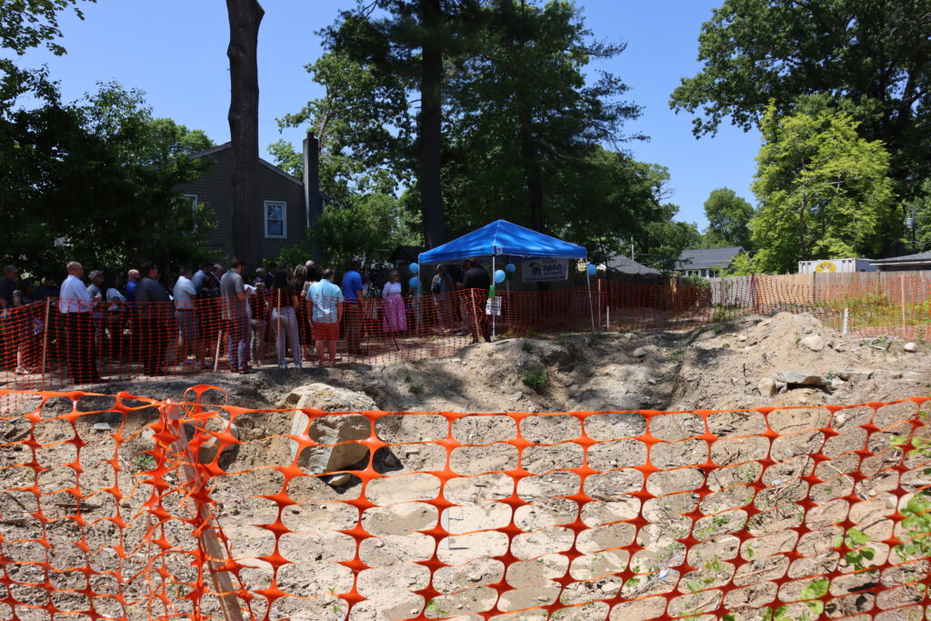 The future site of the habitat for humanity project is shown with the groundbreaking ceremony taking place beyond it.