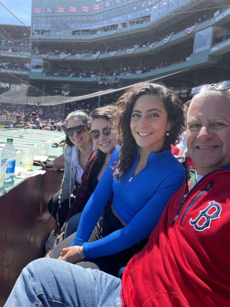 Man in Red Sox shirt sits with three women. Appears to be at Fenway Park.