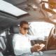Man in sunglasses looks at his cell phone while driving a car.