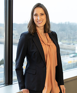 Attorney Sarah C White, of Keches Law Group, is a white-appearing woman with brown hair. She is smiling, wearing an orange shirt and black suit jacket while posing in front of a window.
